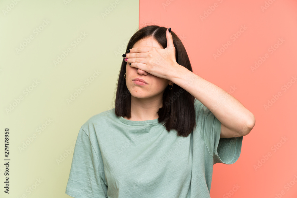 Young woman over isolated colorful wall covering eyes by hands Young woman over isolated colorful wall covering eyes by hands