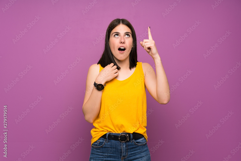 Young woman over isolated purple wall pointing up and surprised Young woman over isolated purple wall pointing up and surprised