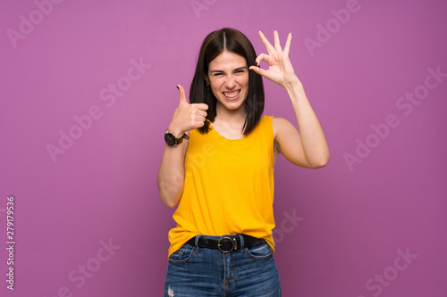 Young woman over isolated purple wall showing ok sign and thumb up gesture