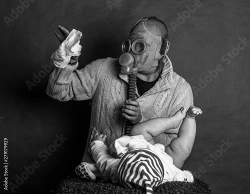 Young Dad cleaning his baby's dirty ass, changing the stinky diaper in a gas mask, fatherhood and humor..Father changes the baby's diapers on a changing table, on a dark, single track background.