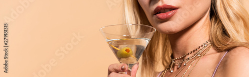 cropped view of elegant blonde woman in necklace holding cocktail isolated on beige, panoramic shot