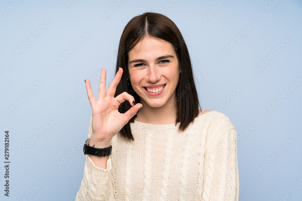 Young woman over isolated blue wall showing an ok sign with fingers Young woman over isolated blue wall showing an ok sign with fingers