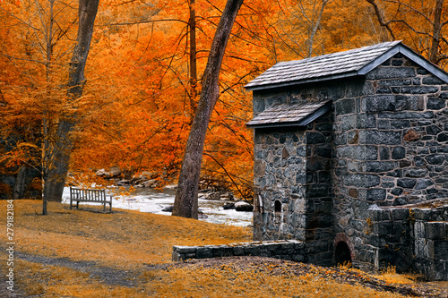 Brick cabin and bench in Autumn forest. Landscape with cabin, river and Autumn trees.