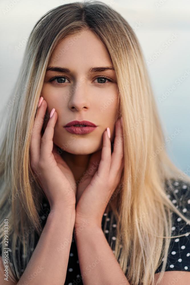 A young attractive blond woman, in a blue dress, walks along the seashore. Portrait of a smiling woman on vacation with a glass of wine.