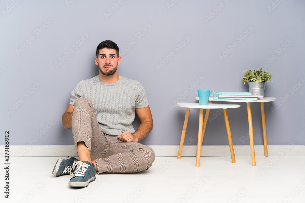 Young handsome man sitting on the floor having doubts and with confuse face expression