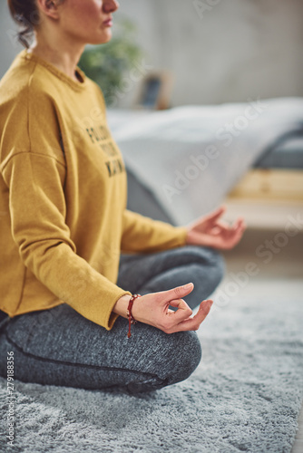 Beautiful Caucasian brunette sitting on rug in bedroom in Lotus yoga posture.