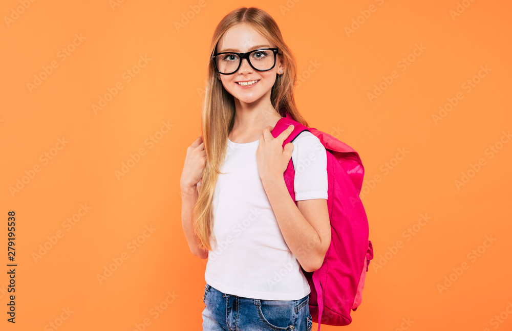 Beautiful smiling and happy school girl with backpack is posing on yellow background