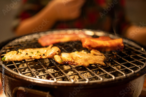 Grilling sliced pork and beef over stove in Japanese style with blurry woman in background