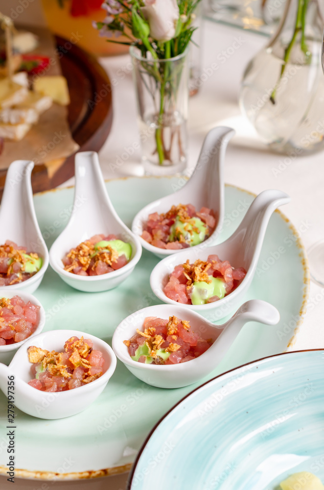 Top view catering banquet table with cold snacks tar tar. Raw salmon tartare decorated cucumber, olives on a serving spoon iIsolated on white background. Party food.