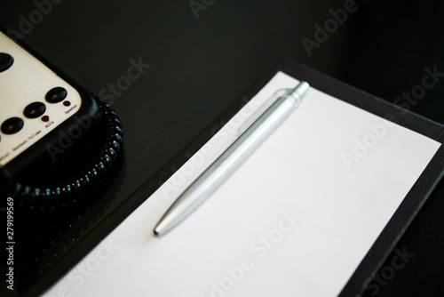the silver pen color is placed on white short note paper on the brown wooden table near telephone in the luxury hotel room