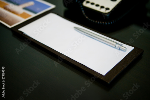 the silver pen color is placed on white short note paper on the brown wooden table near telephone in the luxury hotel room