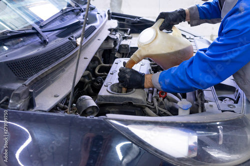 Car mechanic replacing and pouring fresh oil into engine with a special container at maintenance repair service station.