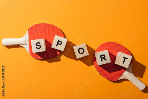 top view of wooden cubes with sport lettering near table tennis rackets on yellow