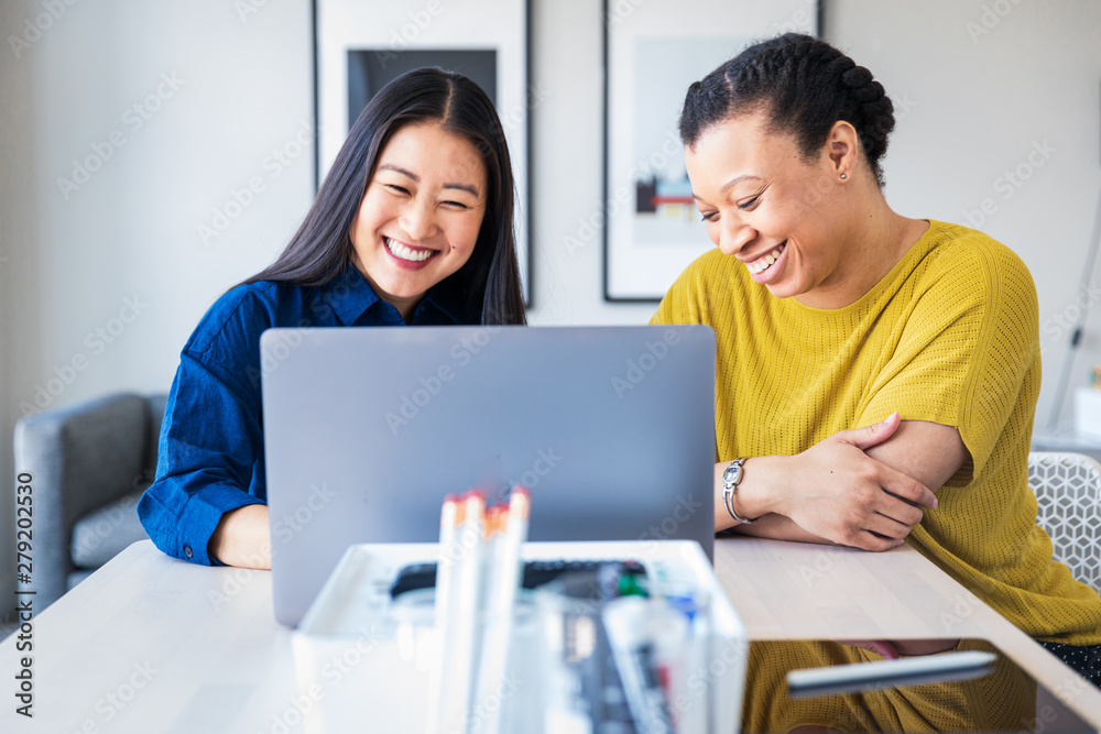 Two business colleagues smiling in front of laptop Two business colleagues smiling in front of laptop