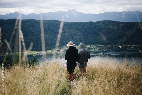 Two man in hiking or camping outdoor outfits stand in middle of alpine field, overlook valley with beautiful lake at bottom during summer vacation in national park © BublikHaus