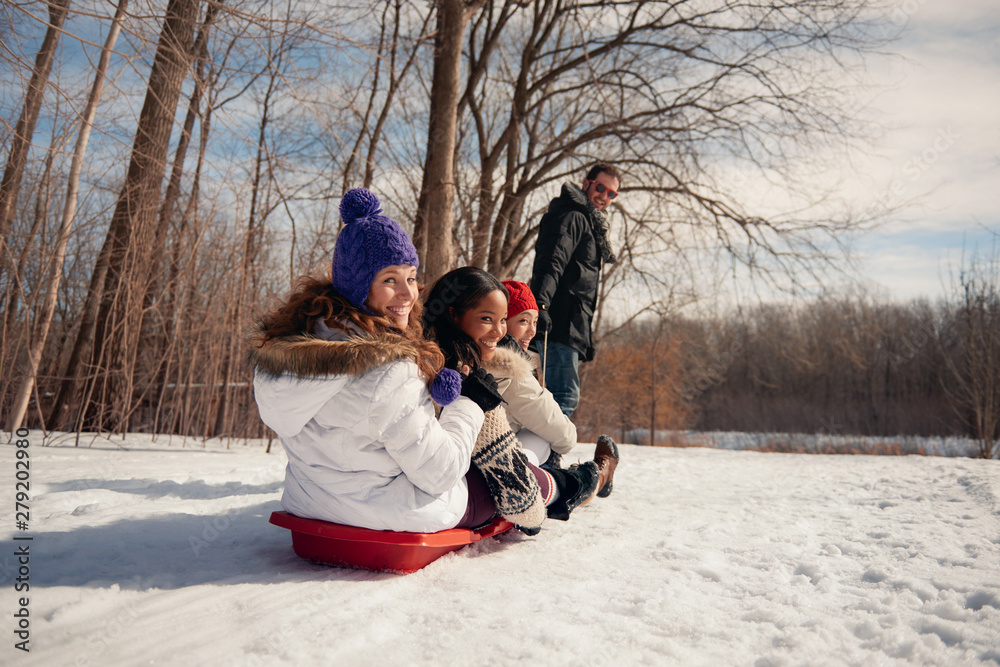 Group of friends enjoying pulling a sled in the snow in winter