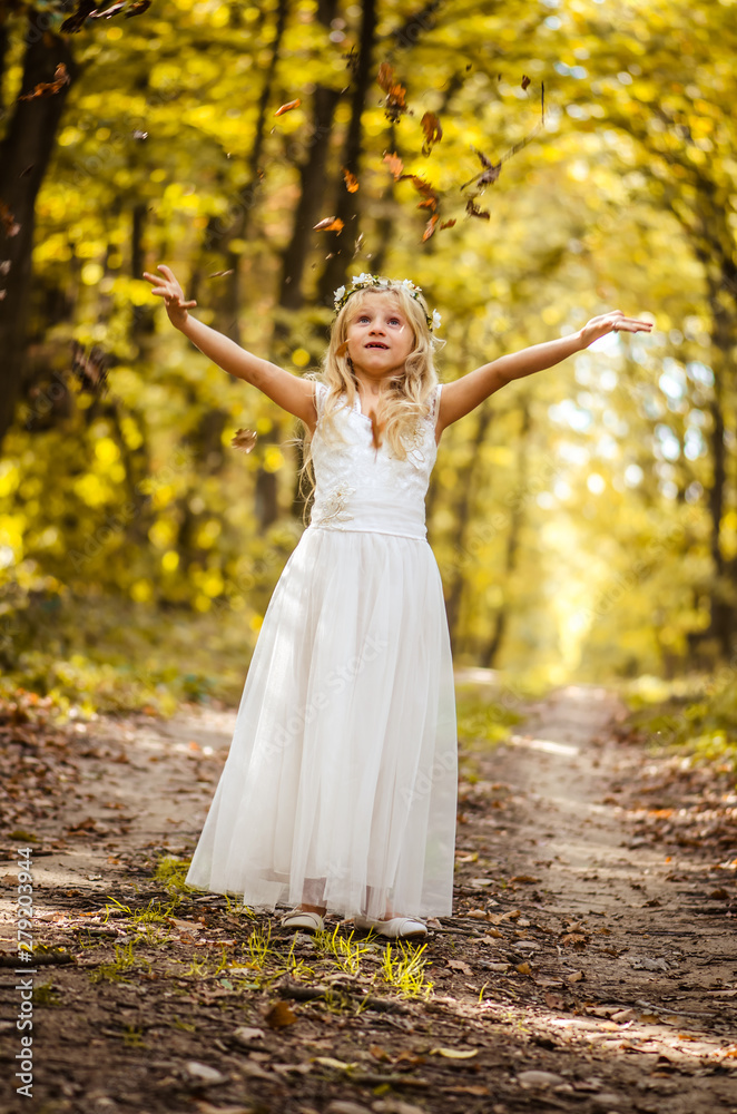 adorable blond girl with leaves in hands in sunny day in magical forest
