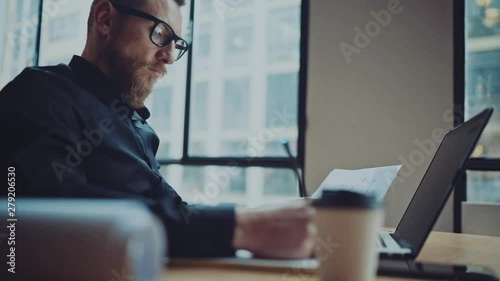 Bearded businessman man working at sunny office on desktop computer while sitting at wooden table.