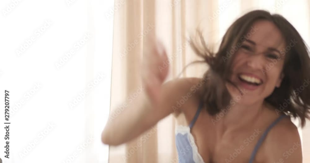 Excited woman in nightwear playing with pillow on bed Excited woman in nightwear playing with pillow on bed