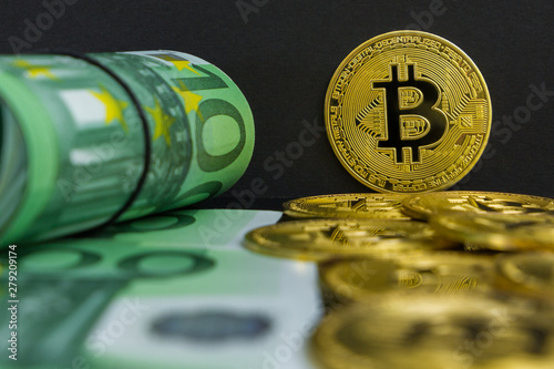 Euro vs bitcoin cryptocurrency. There are one hundred euro banknotes and big golden btc coins on a black background. Golden bitcoin over Euro money photo