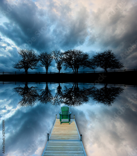 Mirror imaged of five trees along a roadway silhouetted against stormy clouds with an Adirondack chair sitting on a dock, Stowe Vermont, USA photo