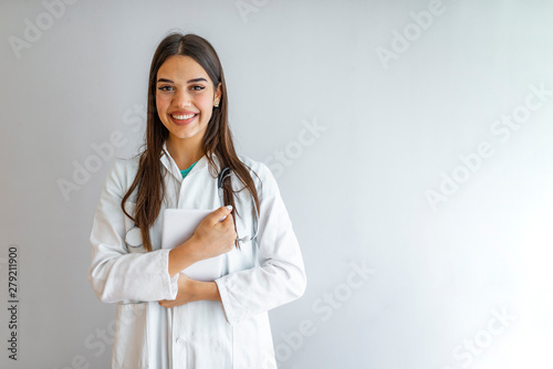 Doctor with digital tablet. Attractive young female doctor in white lab coat working on digital tablet and smiling while standing against grey background
