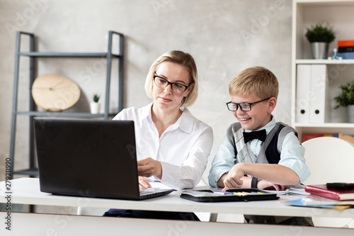 Wallpaper Mural Young schoolboy in sweater and his charming teacher in white blouse sit behind desk and working with laptop Torontodigital.ca