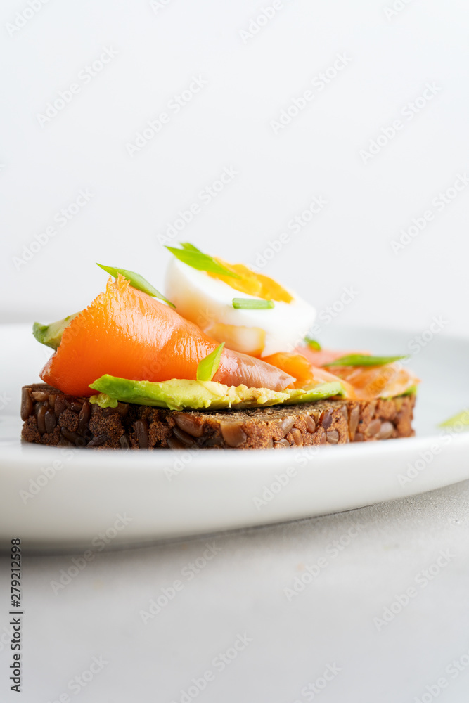 Healthy open sandwiches on multigrain wholegrain  toast with avocado, salmon, eggs, herbs, sunflower seeds over white plate on concrete background with copy space. Healthy protein food.