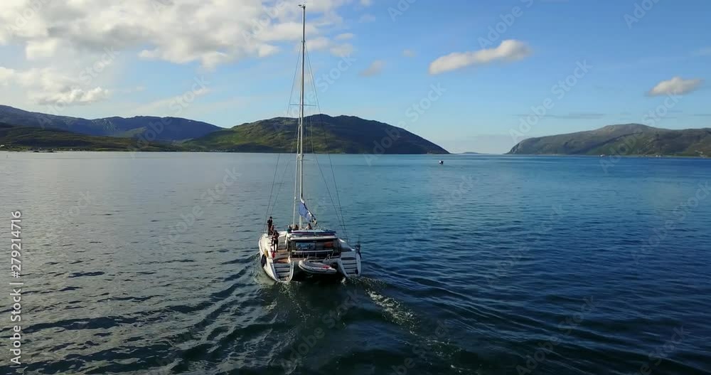 Aerial, drone shot panning a catamaran sailboat, sailing in tranquil waters, on the coast of Senja, on a sunny summer day, in Troms, north Norway Aerial, drone shot panning a catamaran sailboat, sailing in tranquil waters, on the coast of Senja, on a sunny summer day, in Troms, north Norway