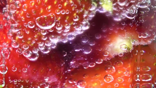 Glass soda water with ice cubes and strawberries, centre screen. Fizzy bubbles rising. Rotating background.