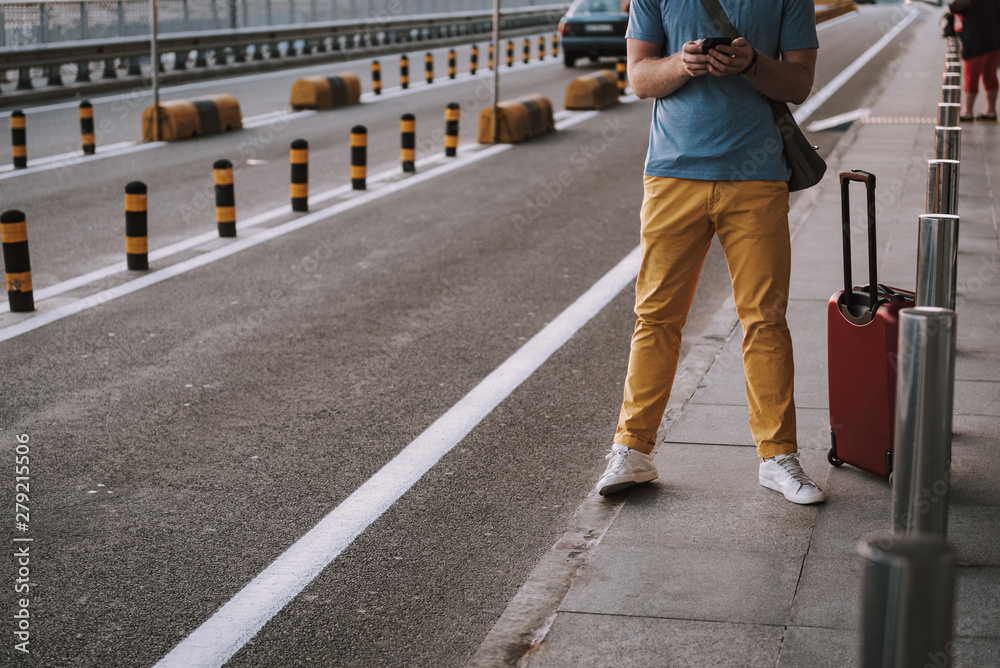 Fototapeta premium Young man with travel bag using cellphone on the street
