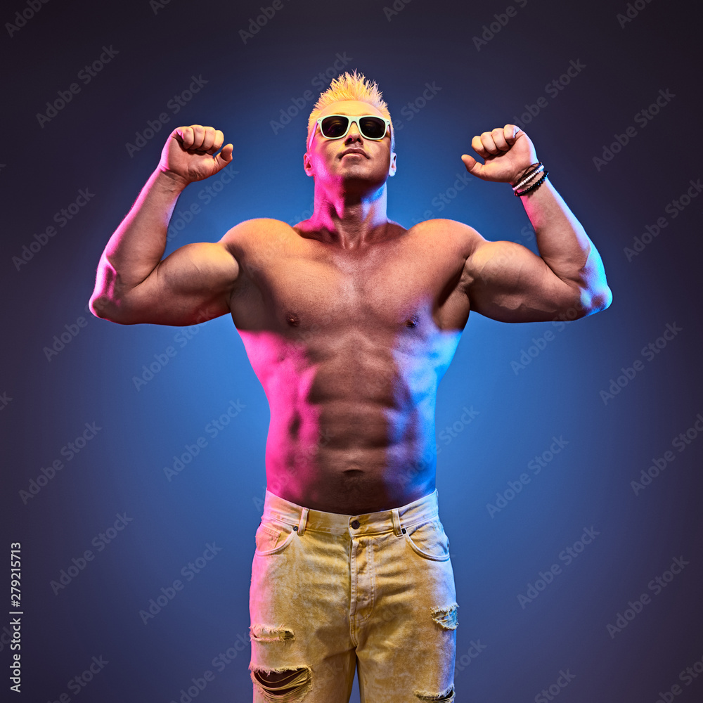Charismatic Muscular man with naked torso jump in colorful neon light. Sexy bodybuilder fitness guy Having Fun on blue background. Healthy naked male athletic body concept. Happy positive motivation