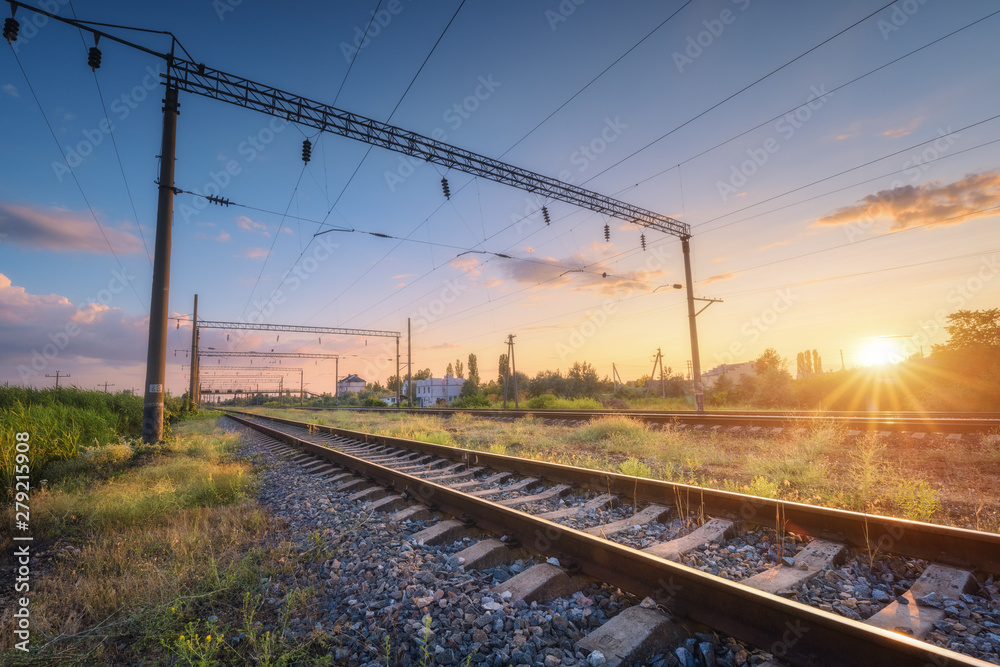 Railway station and beautiful sky at sunset. Summer rural industrial landscape with railroad, blue sky with colorful clouds and sunlight, green grass. Railway platform. Transportation. Heavy industry