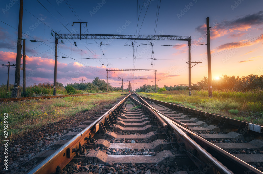 Railway station and beautiful sky at sunset. Summer rural industrial landscape with railroad, blue sky with colorful clouds and sunlight, green grass. Railway platform. Transportation. Heavy industry