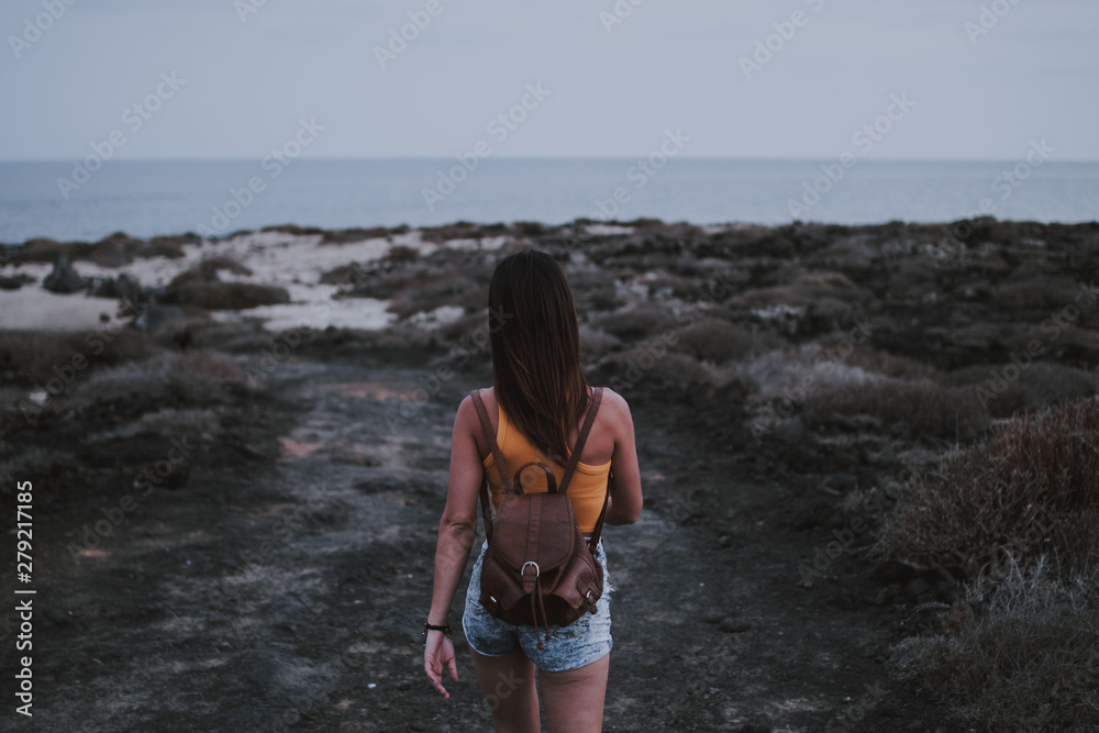 Chica caminando de espaldas por costa volcánica de piedras en la isla de Lanzarote
