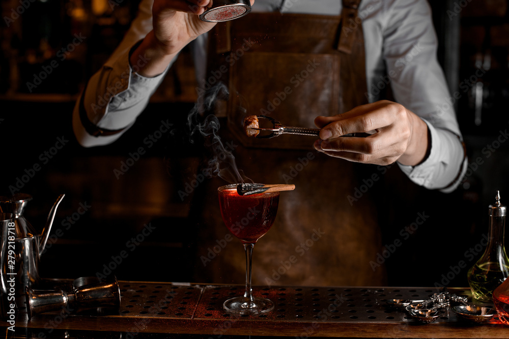 Bartender add spices for a decor above a delicious red cocktail in the glass