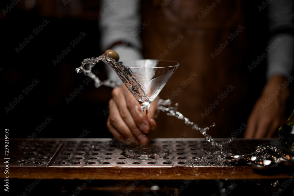 Male bartender mixing a transparent alcoholic drink in the martini glass with one olive