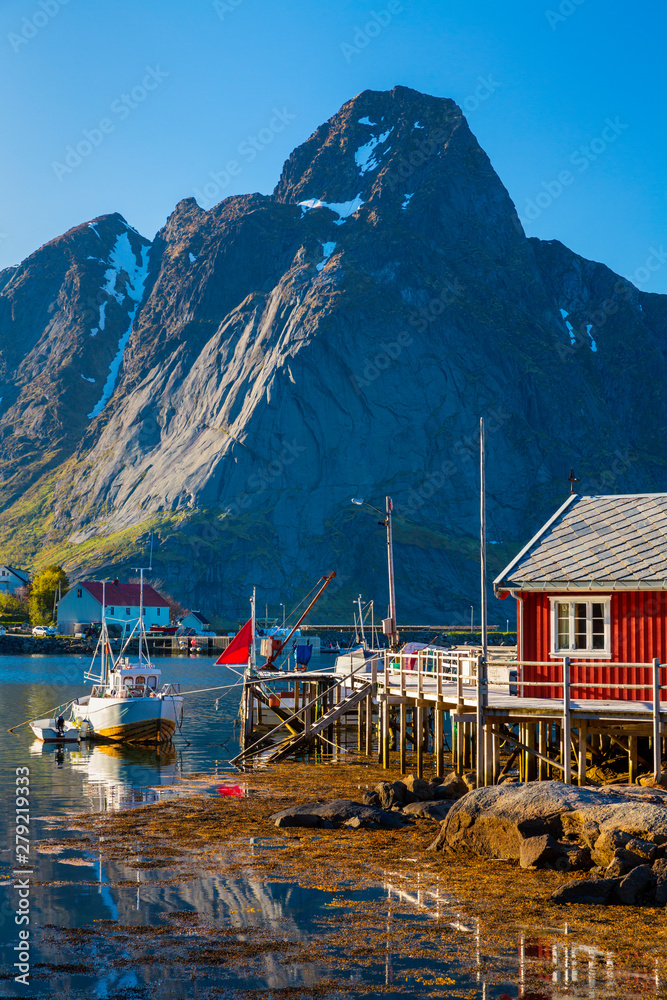 Reine Village on the Lofoten Islands,  Norway. The Typical Norwegian fishing village of Reine under midnight sun,  with the typical rorbu houses.  Mountain In Background