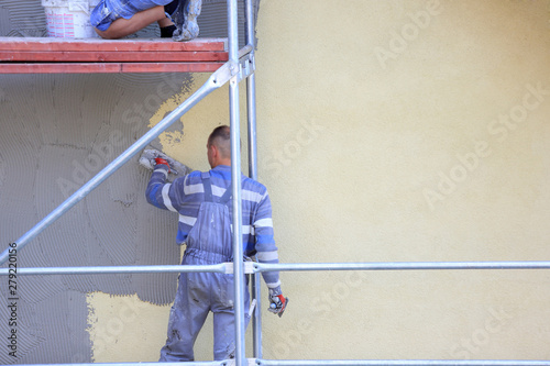 Tynkarze na rysztowaniu w trakcie nakładania tynku na ścianę budynku.