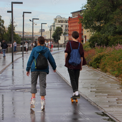 Russia / Moscow, Two girls in autumn clothes rollerblading and skateboarding on the wet sidewalk in the Park Muzeon after the rain photo