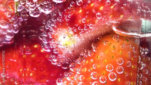 Glass soda water with ice cubes and strawberries, centre screen. Fizzy bubbles rising. Rotating background.