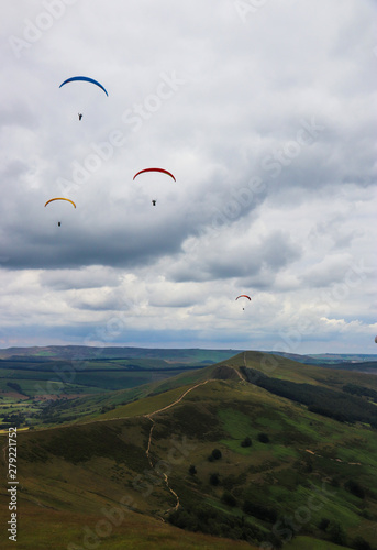 Group of paragliders flying above valley with green mountain and clouds in the background