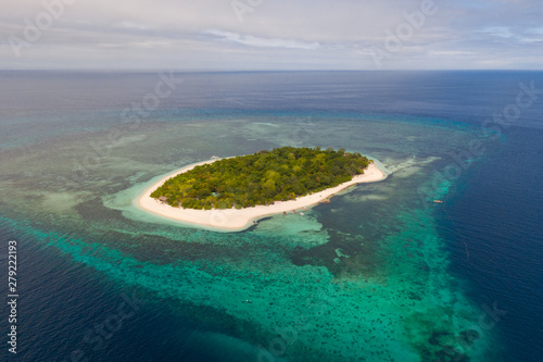 A small island surrounded by azure water and coral reefs, a top view.Round tropical island with white sandy beach, top view.Mantigue Island, Philippines.