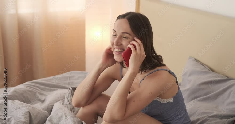 Young woman in nightdress having fun while talking on mobile phone in bed Young woman in nightdress having fun while talking on mobile phone in bed