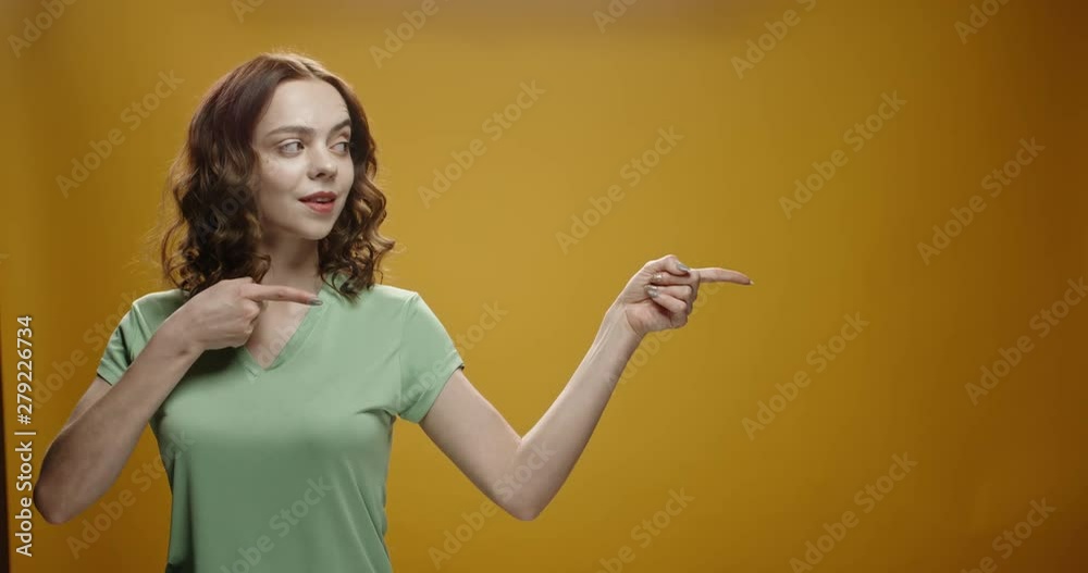 Caucasian model positively smiling, pointing in air and gesturing positive signs, isolated on yellow background. A template for your graphics close up 4k footage Caucasian model positively smiling, pointing in air and gesturing positive signs, isolated on yellow background. A template for your graphics close up 4k footage