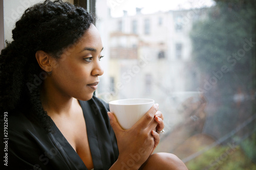 Canvas Print Woman looking through window holding coffee cup