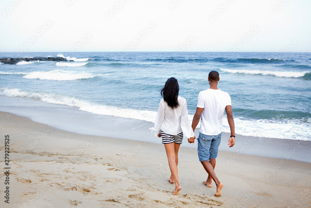 Obraz premium Young couple walking on beach holding hands