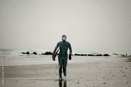 Portrait of man in wetsuit with surfboard running on beach