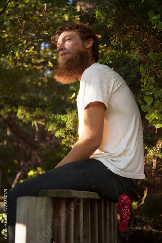Young man sitting on wooden railing under lush foliage