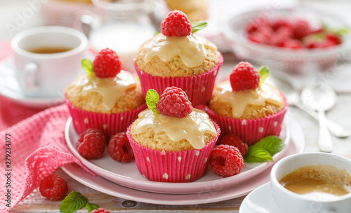 Cupcakes with white chocolate and fresh raspberries on a ceramic plate on a wooden white table, close up. A delicious dessert or breakfast.